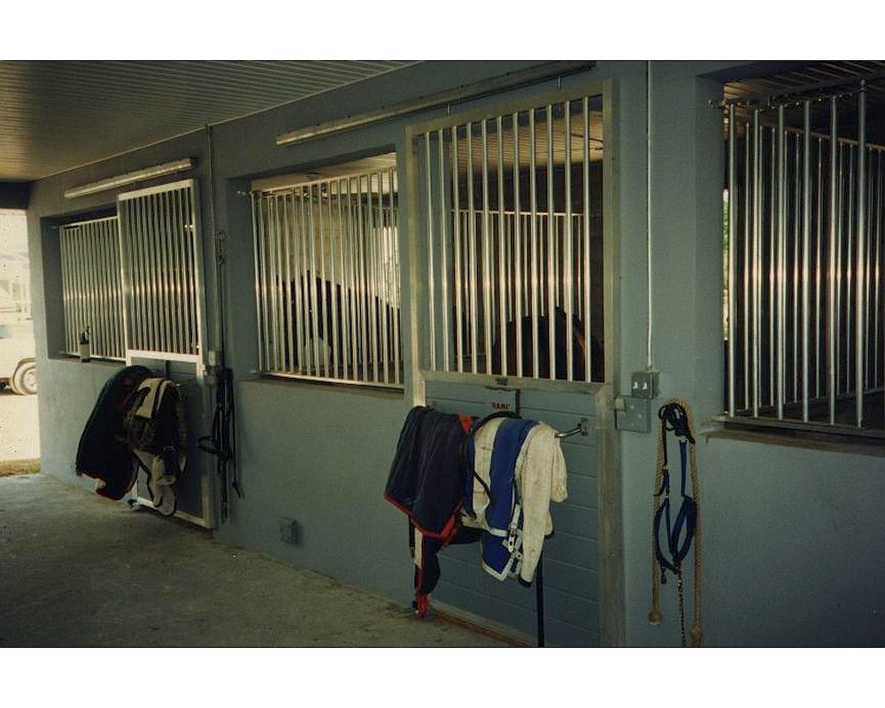 Concrete block barn with aluminum sliding horse stall doors and front grills.